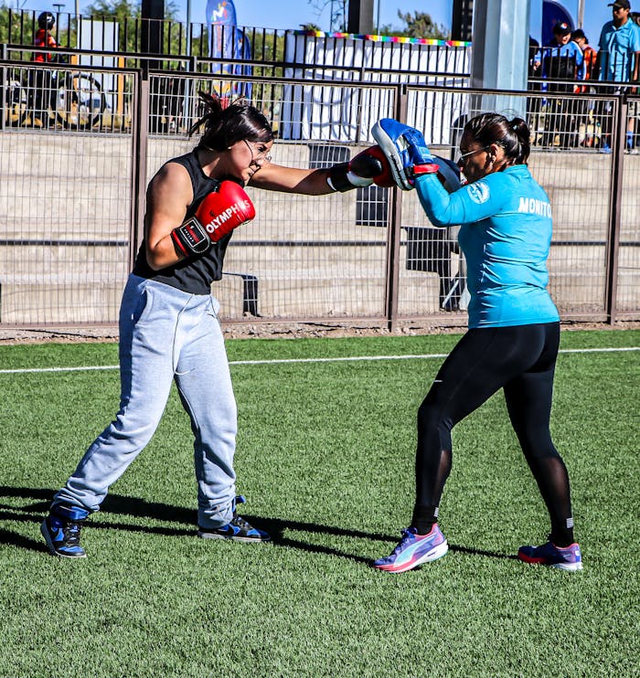 Two women practicing boxing outside on a sunny day with gloves and mitts.